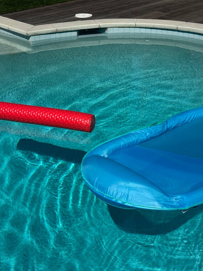 Vibrant summer pool with blue inflatable and red float under bright daylight.